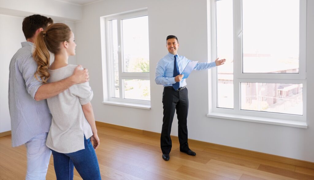 A Realtor pointing to a window inside of an apartment unit to a man and woman.